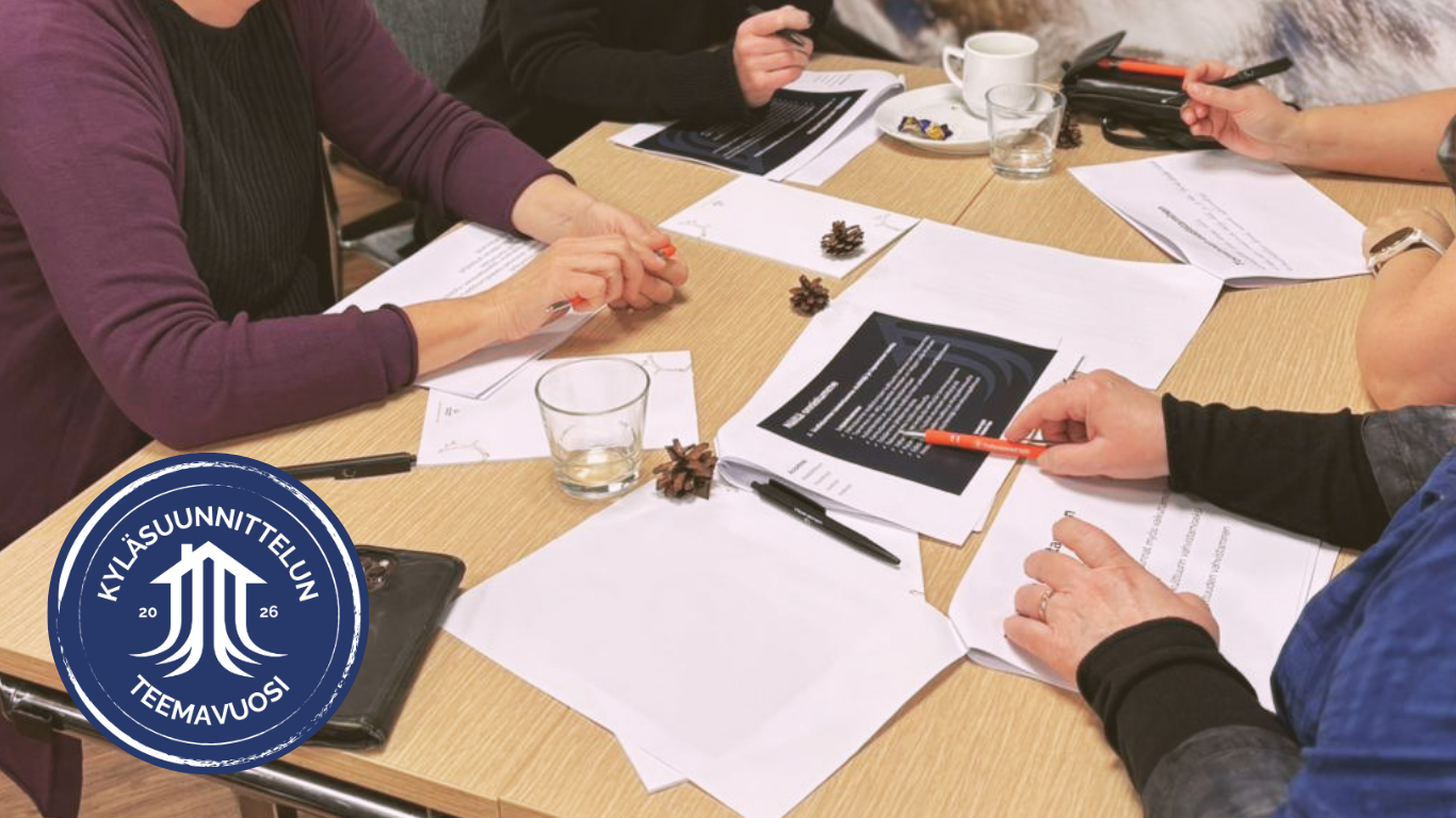 Kuvassa on pöytä ja sen ympärillä ihmisiä. Vain heidän pöydällä olevat kätensä näkyvät. Pöydällä on paperia ja kyniä.